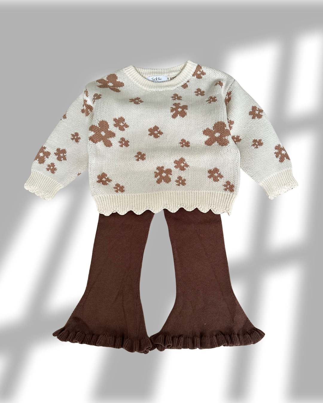 Children's outfit with floral-patterned sweater and brown pants on a gray background