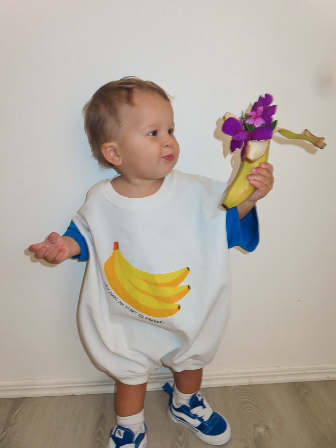 Child wearing a banana-themed outfit holding a banana with flowers. Toddler wearing banana print cotton outfit, playful Aussie kidswear
