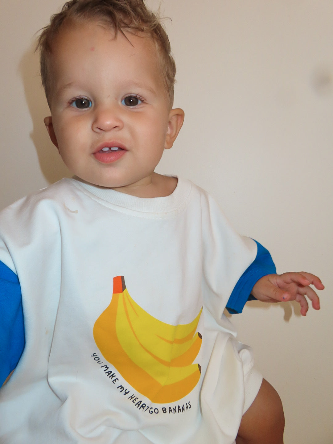 A baby wearing a white romper with a banana print and the text 'you make my heart go bananas' on the front.
